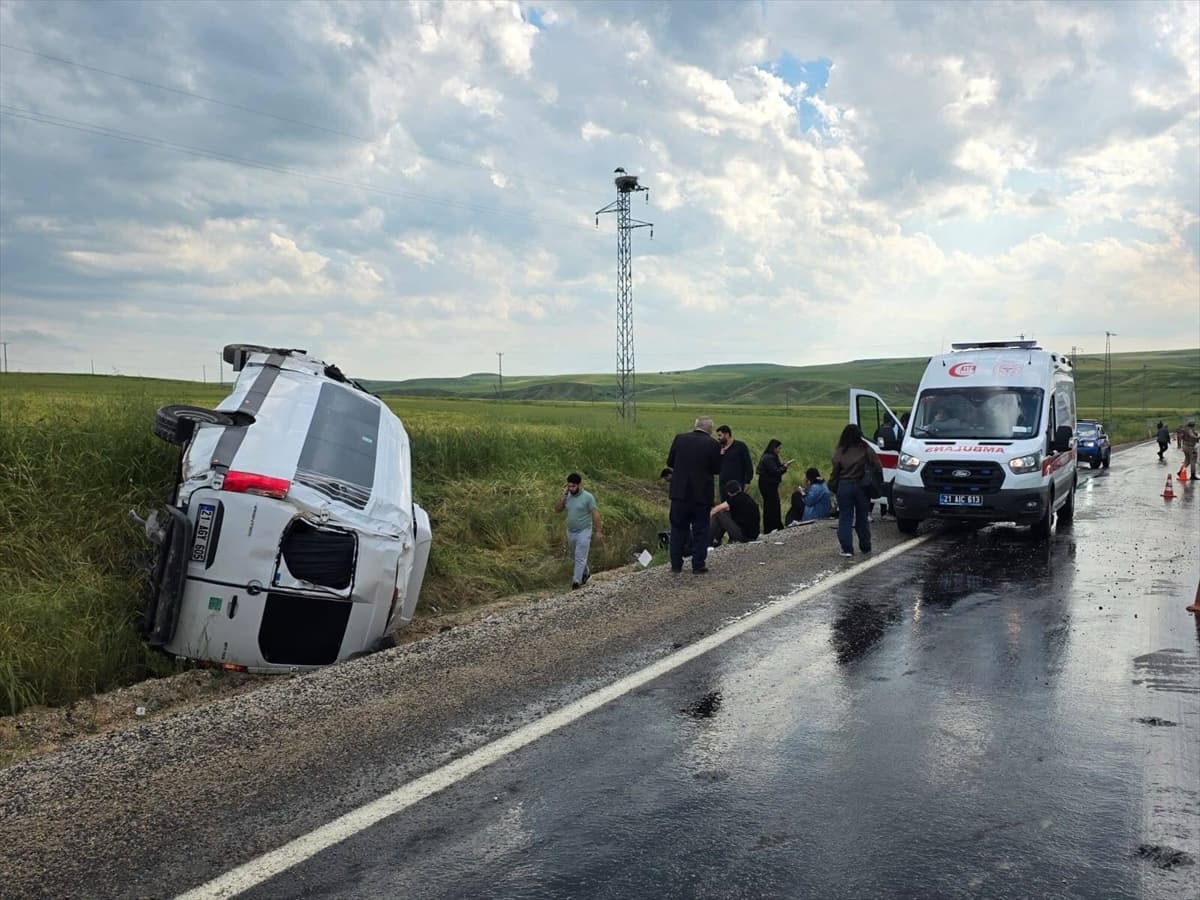Islak yolda devrilmiş beyaz bir minibüs, ambulans ve olay yerinde toplanmış insanlar.
