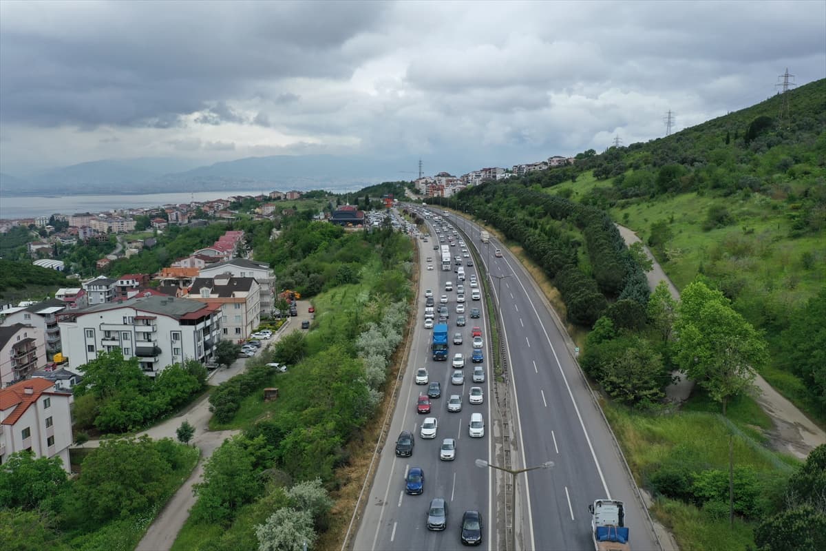 Bulutlu havada, yoğun trafiğin olduğu bir otoyol, solunda şehir ve deniz, sağında yeşil tepeler.