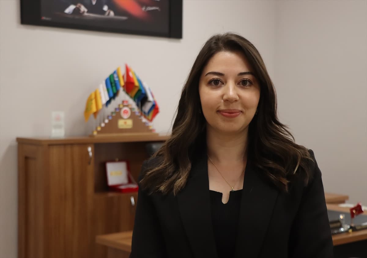 Ofis ortamında, siyah blazer giymiş, hafifçe gülümseyen genç bir kadın.