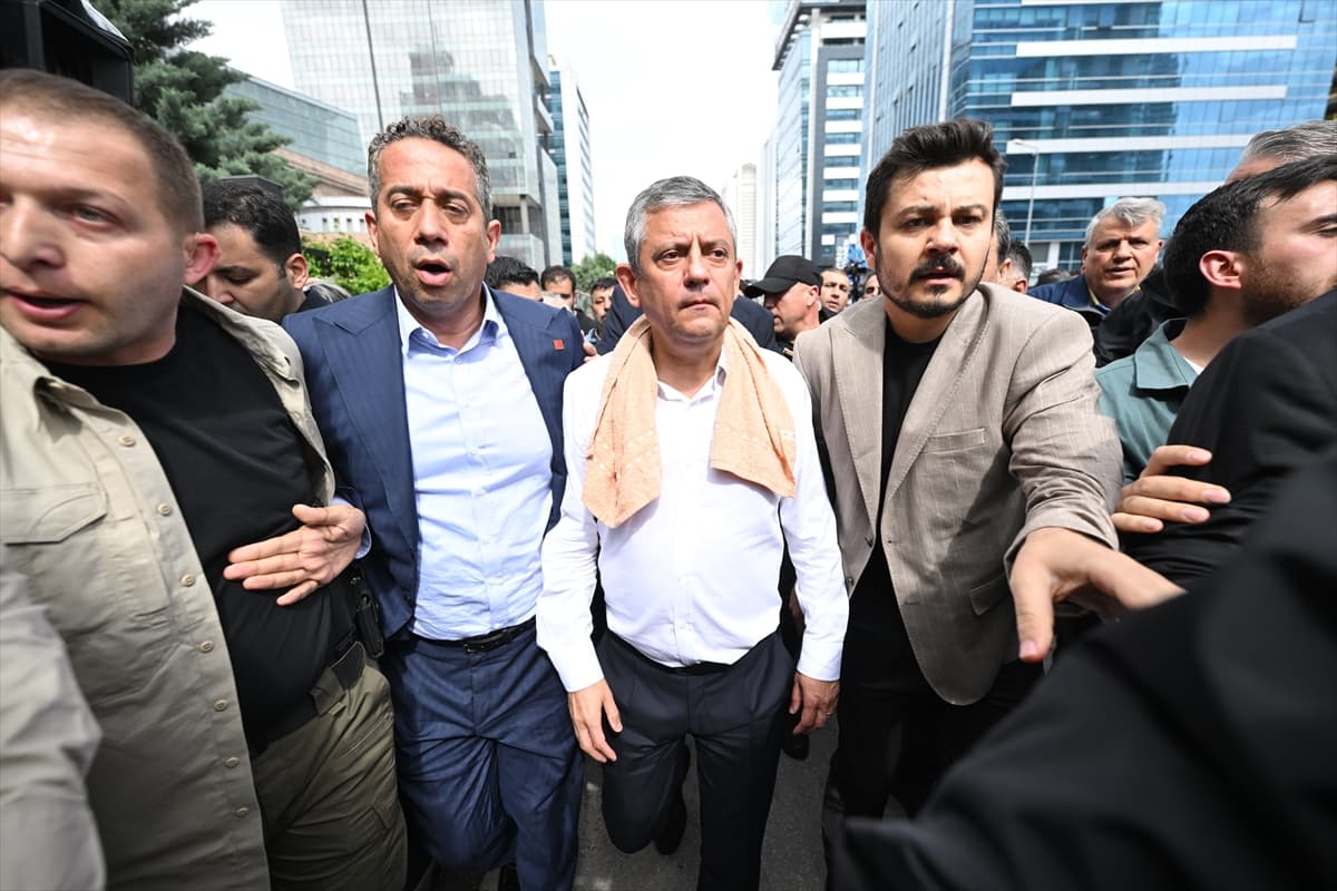 Kalabalık bir ortamda yürüyen, aralarında boynunda havlu olan bir kişinin de bulunduğu bir grup erkek.