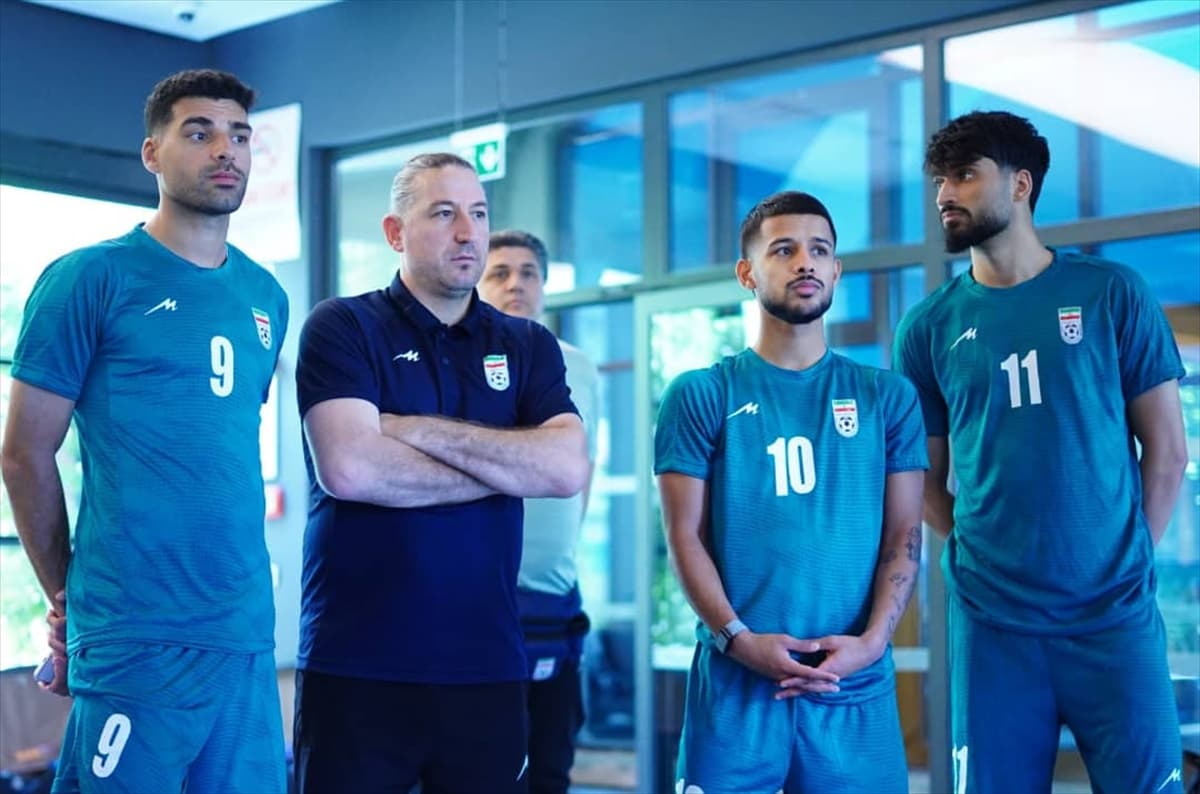 İran milli takımından üç futbolcu ve bir antrenör, formalarıyla kapalı bir alanda ciddi bir ifadeyle duruyor.